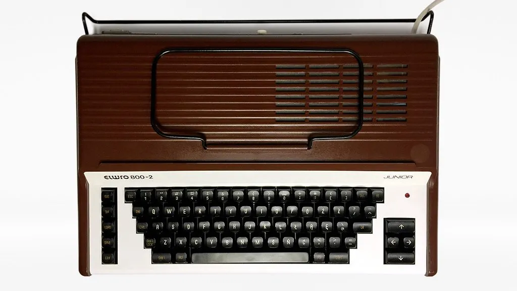 Клон Elwro 800-2 Junior: коричневий корпус із ребристою кришкою, білою панеллю клавіатури, темними клавішами, підписами «elwro 800-2» та «JUNIOR» і окремими клавішами-стрілками праворуч.