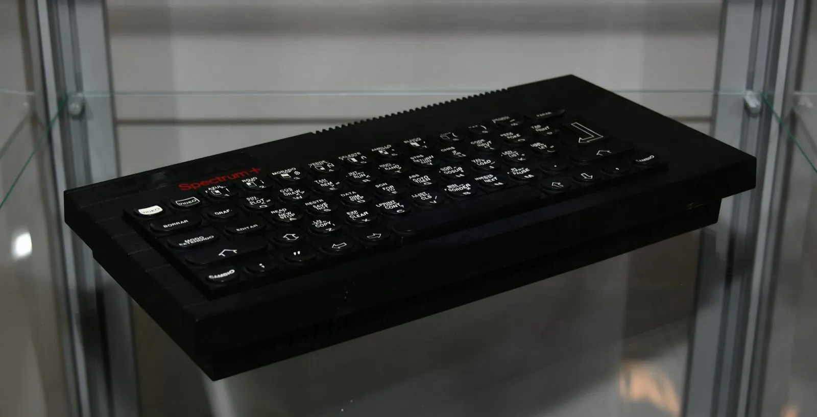 Клон Inves Spectrum + у вітрині: чорний корпус у стилі ZX Spectrum+, червоний напис «Spectrum+» та іспанські підписи клавіш (BORRAR, EDITAR, VIDEO, CAMBIO). Стоїть на скляній полиці.